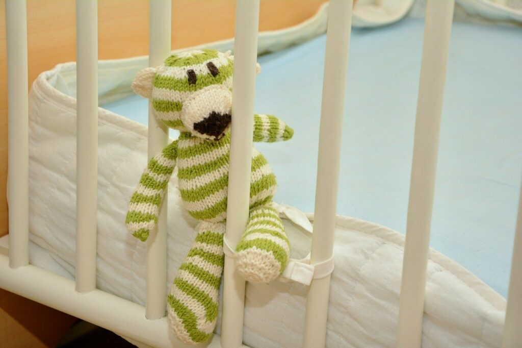 weiß grün gestreiftes Stofftier zwischen den Gittern eines Kinderbettes