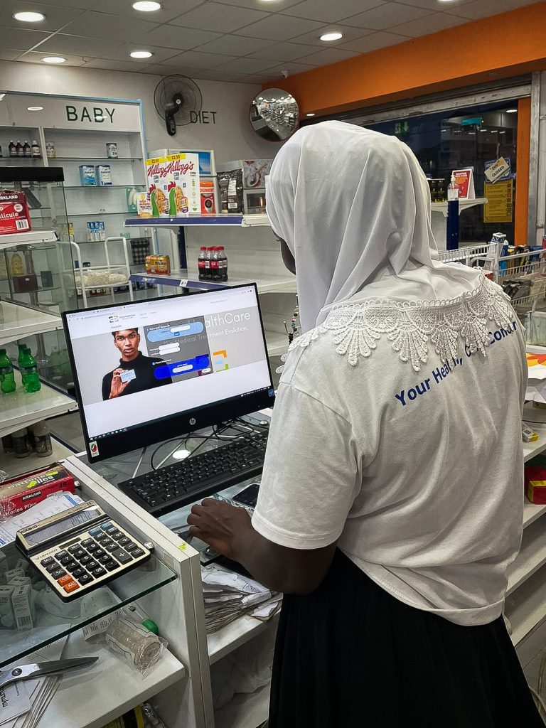 Eine ghanaische Apothekerin steht vor einem Bildschirm und loggt sich bei COMESO ein.