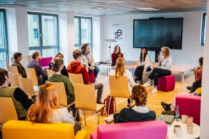 Podiumsdiskussion: die vier Gäste sitzen im Halbkreis zueinander, das Publikum sitz um sie herum mit dem Rücken zur Kamera.